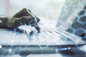 Creative concept of wireless technology with hexagon hologram and hands typing on laptop on background. Big data and database concept. Multiexposure
