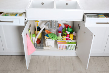 Open under sink cabinet with different cleaning supplies in kitchen
