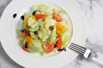 Salad with cabbage, tomatoes, cucumber, pumpkin in a plate on the marble table. Breakfast