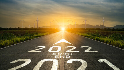 New year 2022 or start straight concept.Word 2022 written on the road in the middle of asphalt road at sunset and destination to wind turbine.Planning,challenge,business strategy,change energy concept