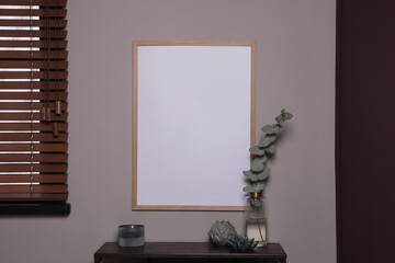 Empty frame hanging on grey wall over wooden table with decor. Mockup for design