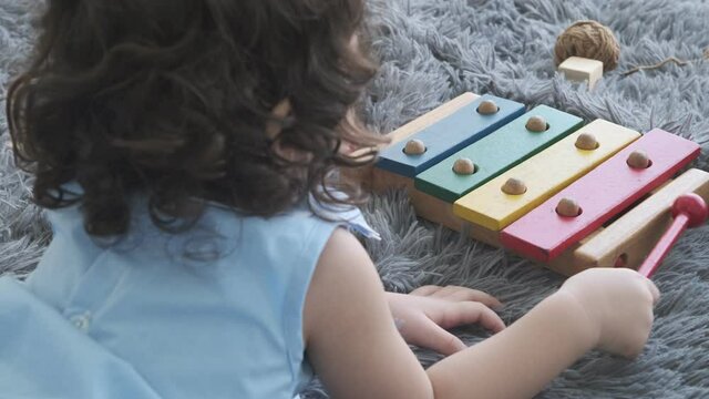 Cute little girl lying on the floor playing wooden xylophone on the floor of the room.