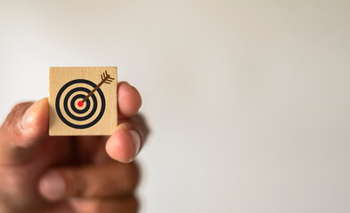 Hand holding wooden cube with arrow target icon on white wall background with copyspace use for...