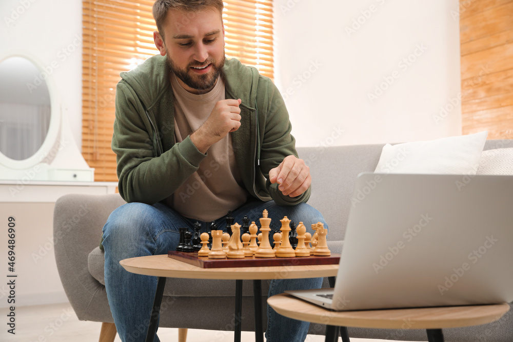 Wall mural young man playing chess with partner through online video chat in living room