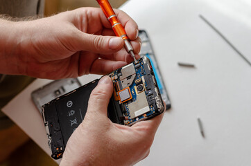 A man is repairing a Smartphone. Hands hold a screwdriver and di