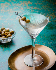 Dirty martini cocktail in martini glass with olives garnish on green colored table - obrazy, fototapety, plakaty