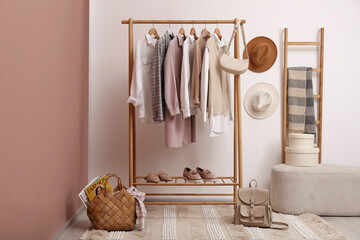 Rack with different stylish clothes and shoes near white wall in room