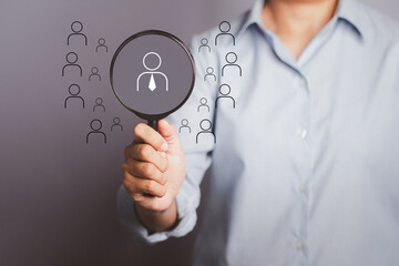 Human resources concept. Officer looking for employee represented by the icon. Hand holding a magnifying glass with people icons over a gray background with copy space for text. Close-up photo