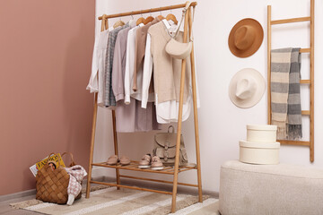 Rack with different stylish clothes and shoes near white wall in room