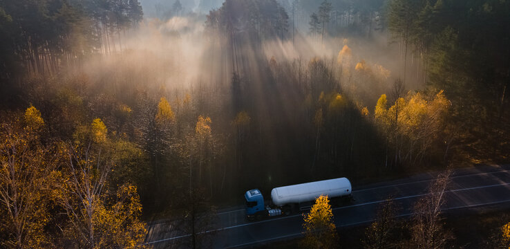 Foggy autumn morning on the road among the woods with a fuel truck passing along the road