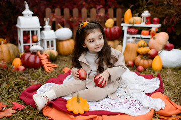 Fototapeta na wymiar Adorable happy baby girl playing in the autumn park. Child playing with pumpkins and apples. Beautiful autumn
