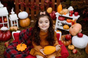 Fototapeta na wymiar Adorable happy baby girl playing in the autumn park. Child playing with pumpkins and apples. Beautiful autumn