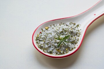 Fragrant seasoning, green salt with a mixture of dried herbs in a ceramic spoon on a white background.