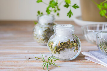 Fragrant seasoning, green salt with a mixture of herbs in a glass jar on a wooden background.