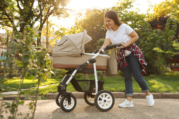 Happy mother with baby in stroller walking in park on sunny day