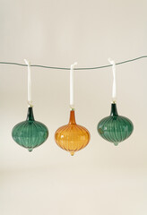 Christmas vintage glass ornaments in orange and green colours hanging on the rope behind pastel beige background. Creative winter holidays and New Year idea. Retro 80s or 90s aesthetic.