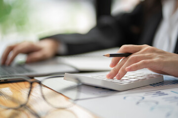 Close-up of businesswoman hand using a calculator to calculate business data, accountancy document at the home office.