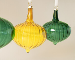 Christmas vintage glass ornaments in vivid yellow and green color hanging on the white rope behind pastel beige background. Winter holidays and New Year composition. Retro 80s or 90s aesthetic.