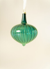 Christmas vintage green glass ornament hanging on white rope behind pastel beige champagne colour background. Minimal winter holidays and New Year concept. Retro 80s or 90s aesthetic.