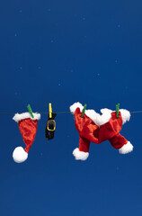 Christmas composition made of Santa's Claus sparkle red clothes hanging on rope behind night blue sky with stars. Winter holidays and New Year idea.