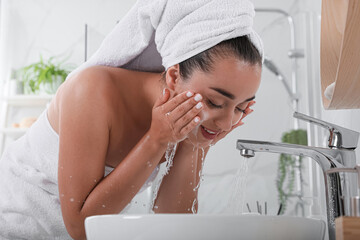 Beautiful young woman washing her face with water in bathroom