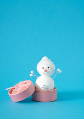 White snowman with snowflake in pink present box against pastel blue background. Winter holidays and New Year gift concept.