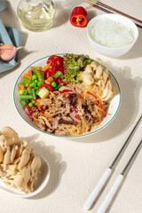Chapche, glass noodles with fried beef, vegetables and oyster mushrooms. Close-up on a light background, with ingredients for cooking, hard shadows