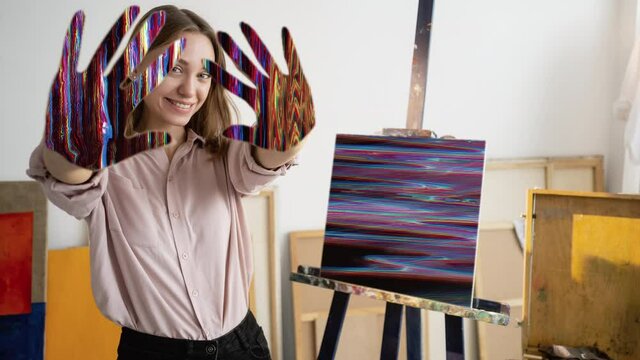 Digital art. Nft painting. Crypto business. Satisfied cheerful female artist with glitch noise animation hands abstract artwork on easel in studio.