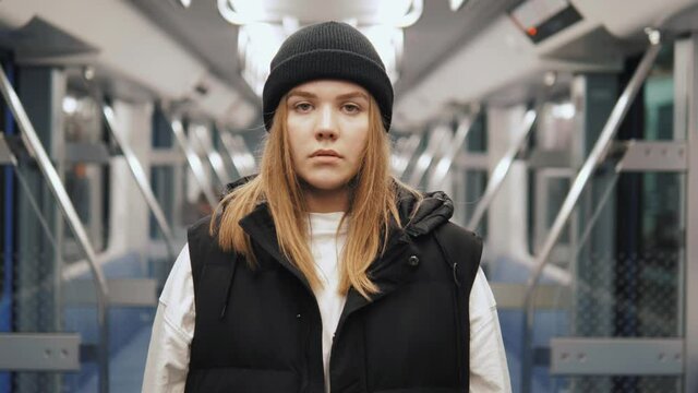 Portrait of pretty confident serious female in black hat standing in subway metro underground. Teenage hipster girl looking at camera in subway transport 