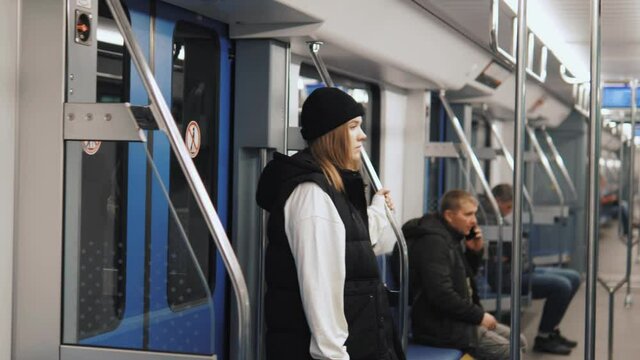 Young pretty female passenger walking in metro waiting standing in a train, holding handrail, going by underground subway tube 