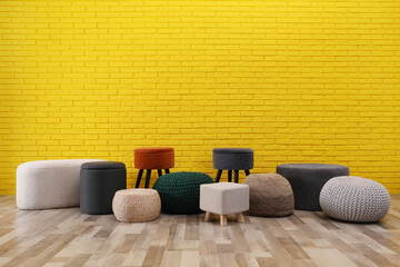 Different stylish poufs and ottomans near yellow brick wall, space for text