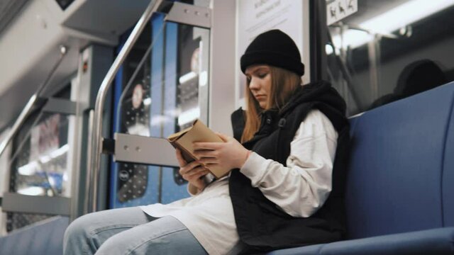 Young isolated focused female sitting in metro and reading an interesting book, self education. Student study in metro while traveling to university school  