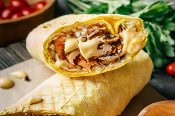 Cheese shawarma with cheese sauce, chicken and vegetables in pita bread on wooden surface, cherry tomatoes and parsley
