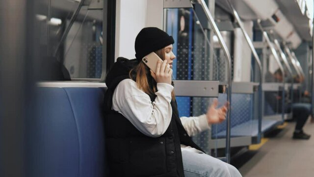 Attractive female hipster in black hat talking having conversation on phone sitting isolated in metro subway underground 