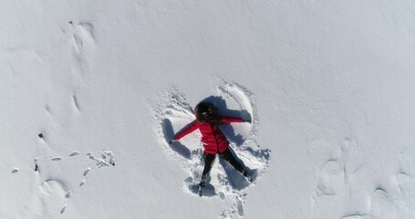 woman lies in the snow and makes an angel