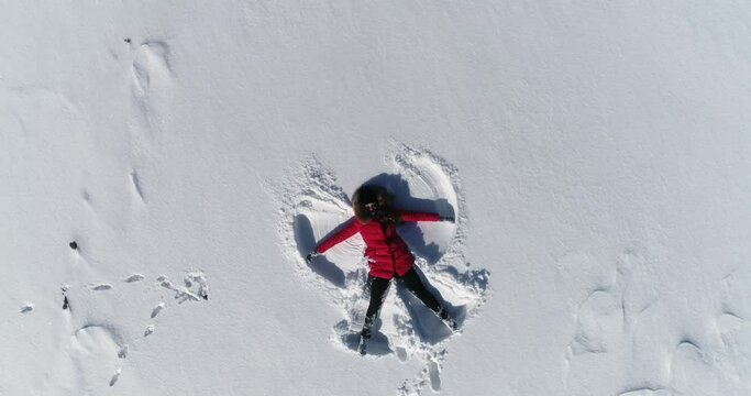 woman lies in the snow and makes an angel