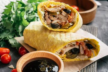 Mexican shawarma with hot sauce, jalapeno pepper, olives on wooden dark surface with cherry tomatoes and green parsley