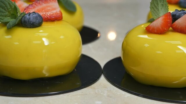 Dolly shot of yellow mousse desserts with strawberries, blueberries and green mint. cakes on dark substrates Covered with mirror glaze