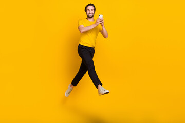 Obraz na płótnie Canvas Full size photo of young guy use cellphone walk jump repost chatting isolated over yellow color background