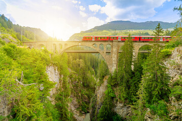 Red train crossing the Solis Viaduct bridge of Swiss railway in Switzerland to Pontresina town....