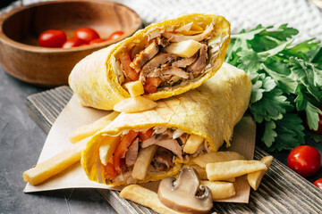 Rustic shawarma with french fries, mushrooms, chicken in pita bread on wooden surface with cherry tomatoes and parsley