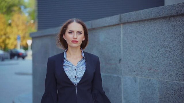 Businesswoman walking city street looking at camera and smile Caucasian female business person walk near corporative building. Modern business woman dressed jacket medium shoot slow motion