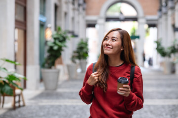 A young asian woman holding coffee cup and walking on the street while traveling and sightseeing around the city