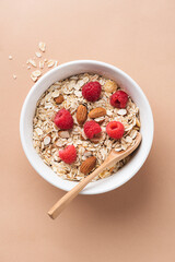 Dry oat muesli with raspberries in bowl isolated on beige background, top view. Healthy breakfast cereals