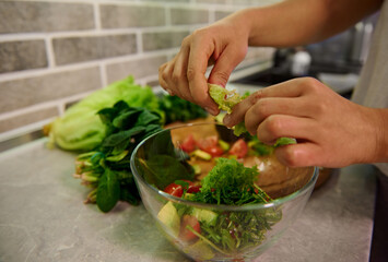 Healthy ingredients for raw vegan salad. Food and concept of veganism, vigor and healthy eating. Close-up of female chef hands preparing raw vegan salad at home kitchen.