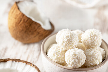 Coconut sweet candies in bowl, broken coconut on light background, selective focus