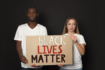 Young woman and African American man holding sign with phrase Black Lives Matter on dark...