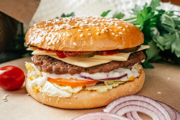 Classic double burger with meat cutlet, lettuce, tomato, pickled cucumber, cheese, onion and sauce on craft paper