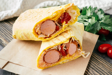 Roll with sausages and vegetables. Hot dog in pita bread on craft paper with cherry tomatoes and green parsley