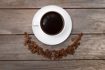 Top view of coffee beans in a shape of smile and coffee cup of espresso on wooden table